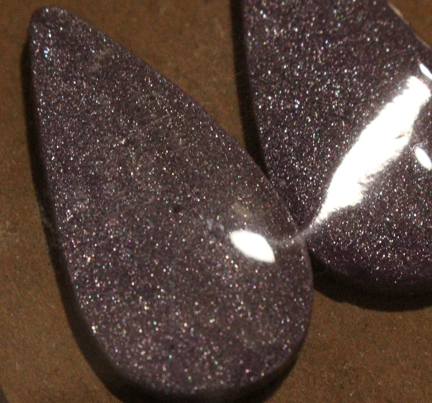 Purple glittery teardrop-shaped earrings on a brown surface