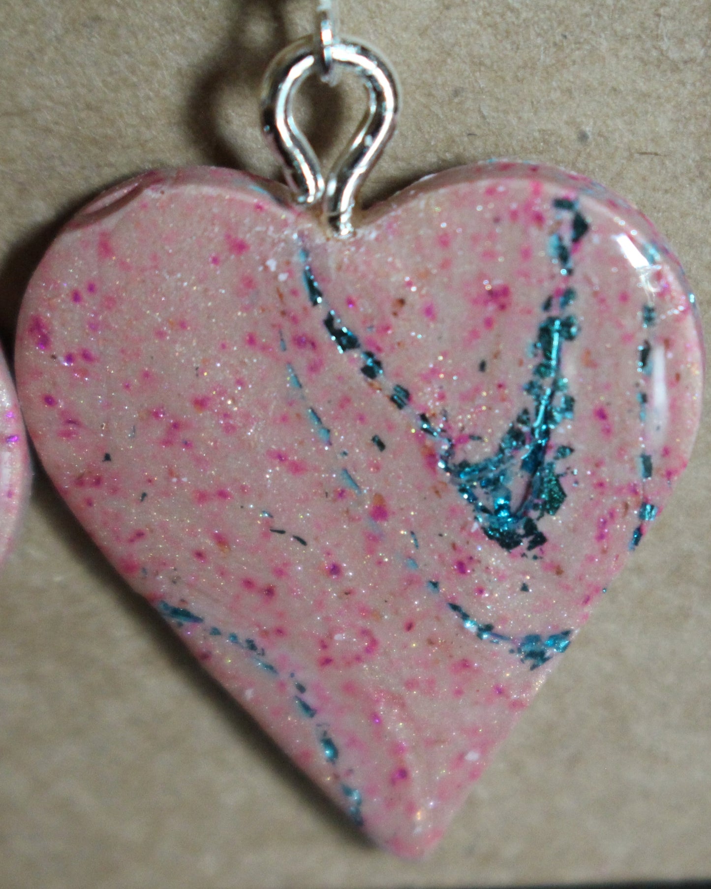 Handmade pink heart-shaped earrings with teal marbling and glitter accents, displayed on a black background.
