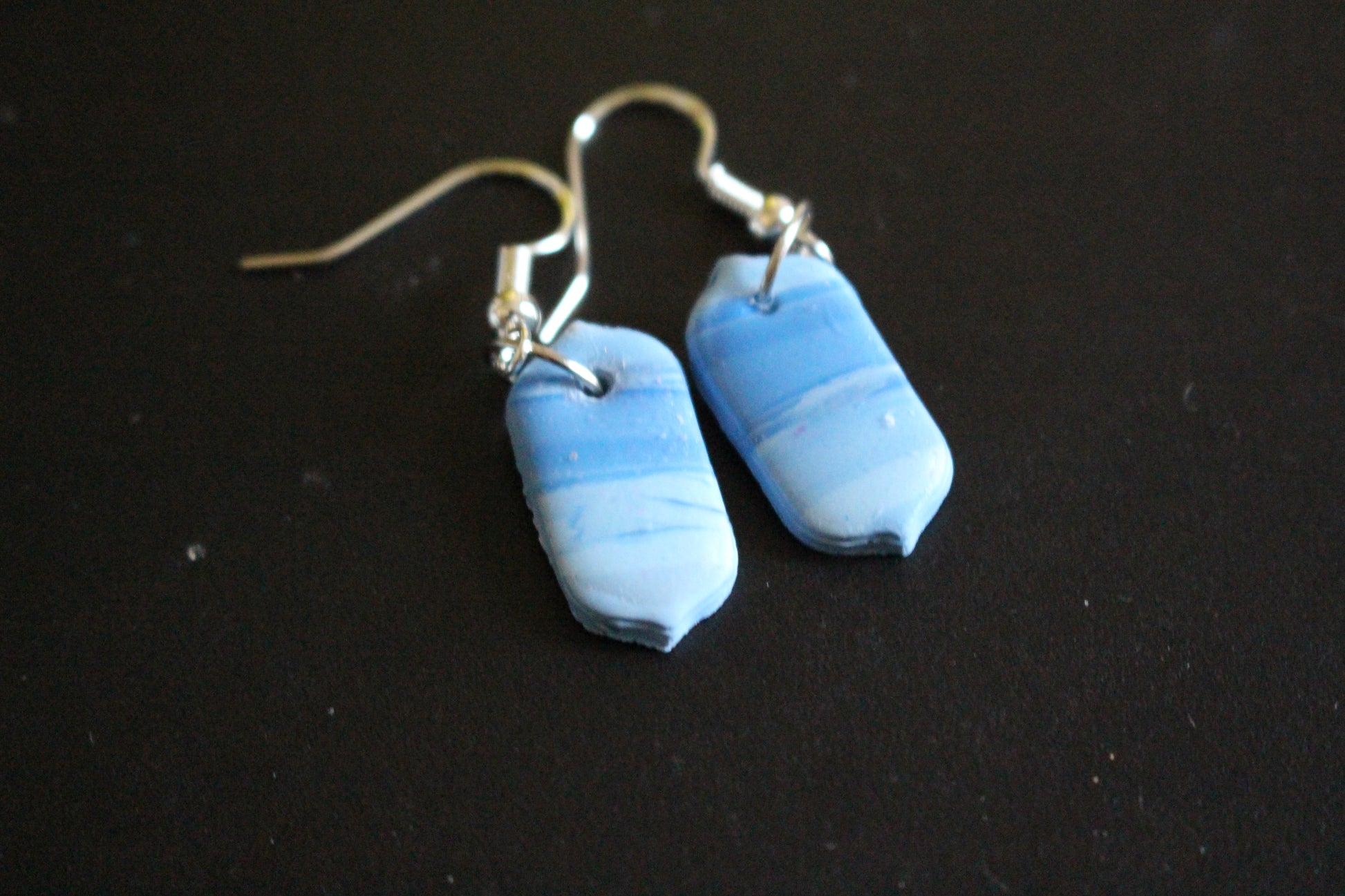 A pair of handcrafted rectangular dangle earrings with a marbled blue and white pattern, displayed on a brown card with silver hooks.