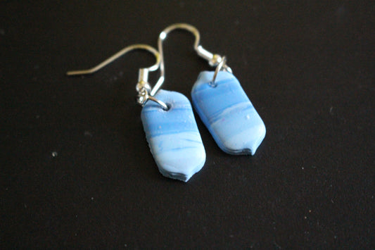 A pair of handcrafted rectangular dangle earrings with a marbled blue and white pattern, displayed on a brown card with silver hooks.