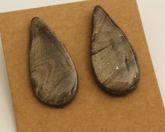 A pair of handcrafted teardrop-shaped earrings in a marbled charcoal gray with a subtle metallic shimmer, displayed on a brown card.