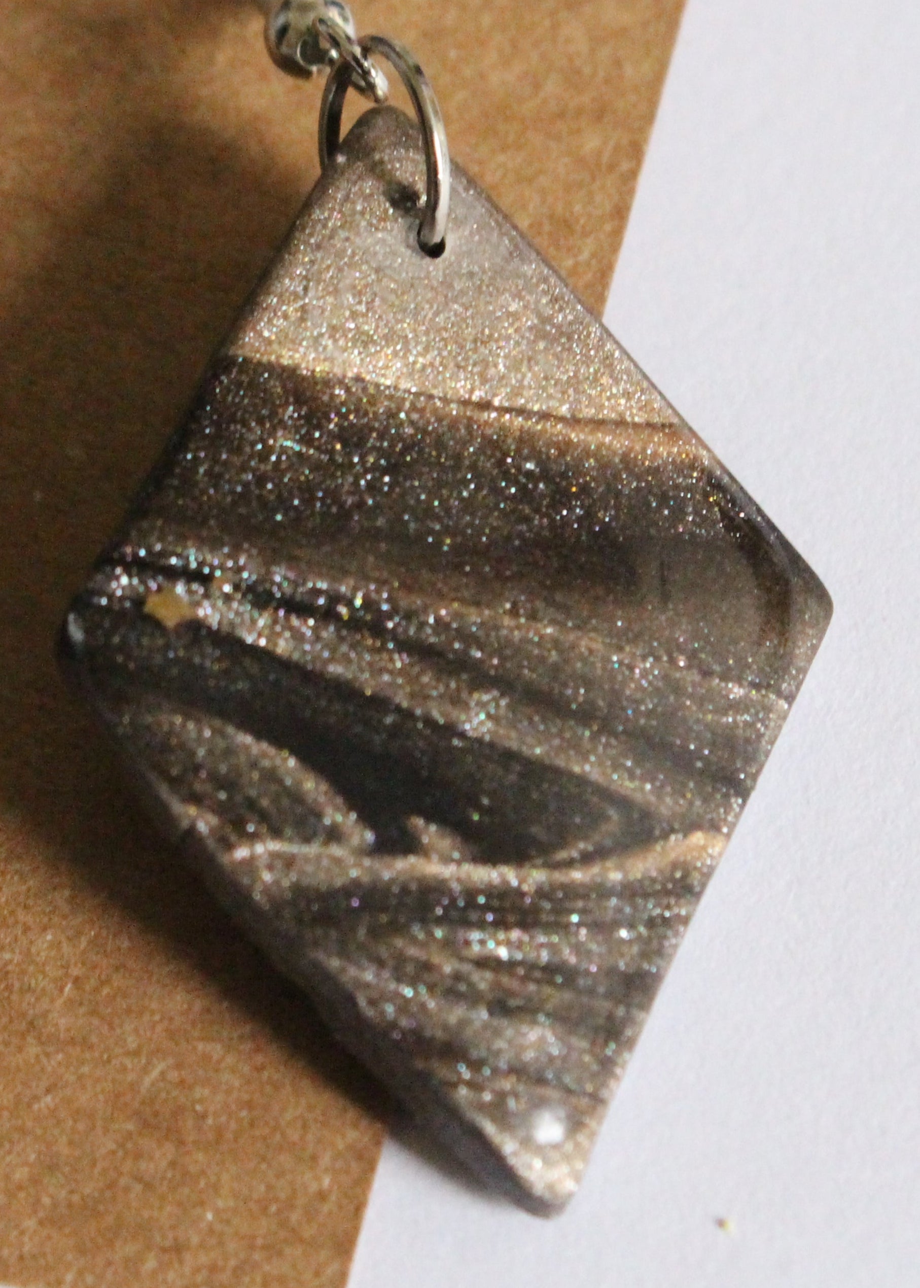 Pair of marbled bronze earrings on a brown card with a white background