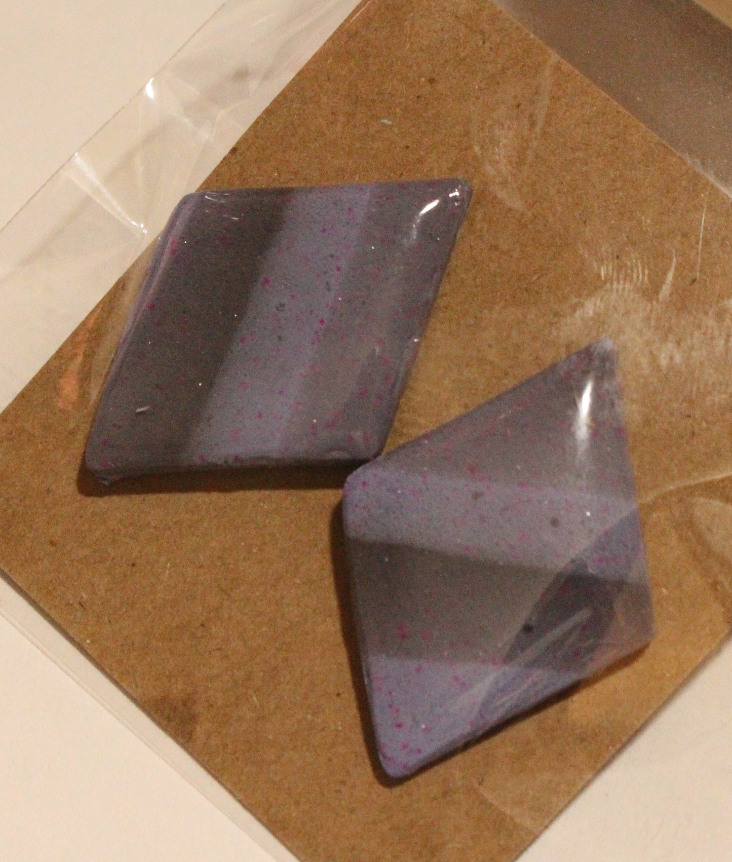 Two purple gemstones on a brown card with clear plastic wrap