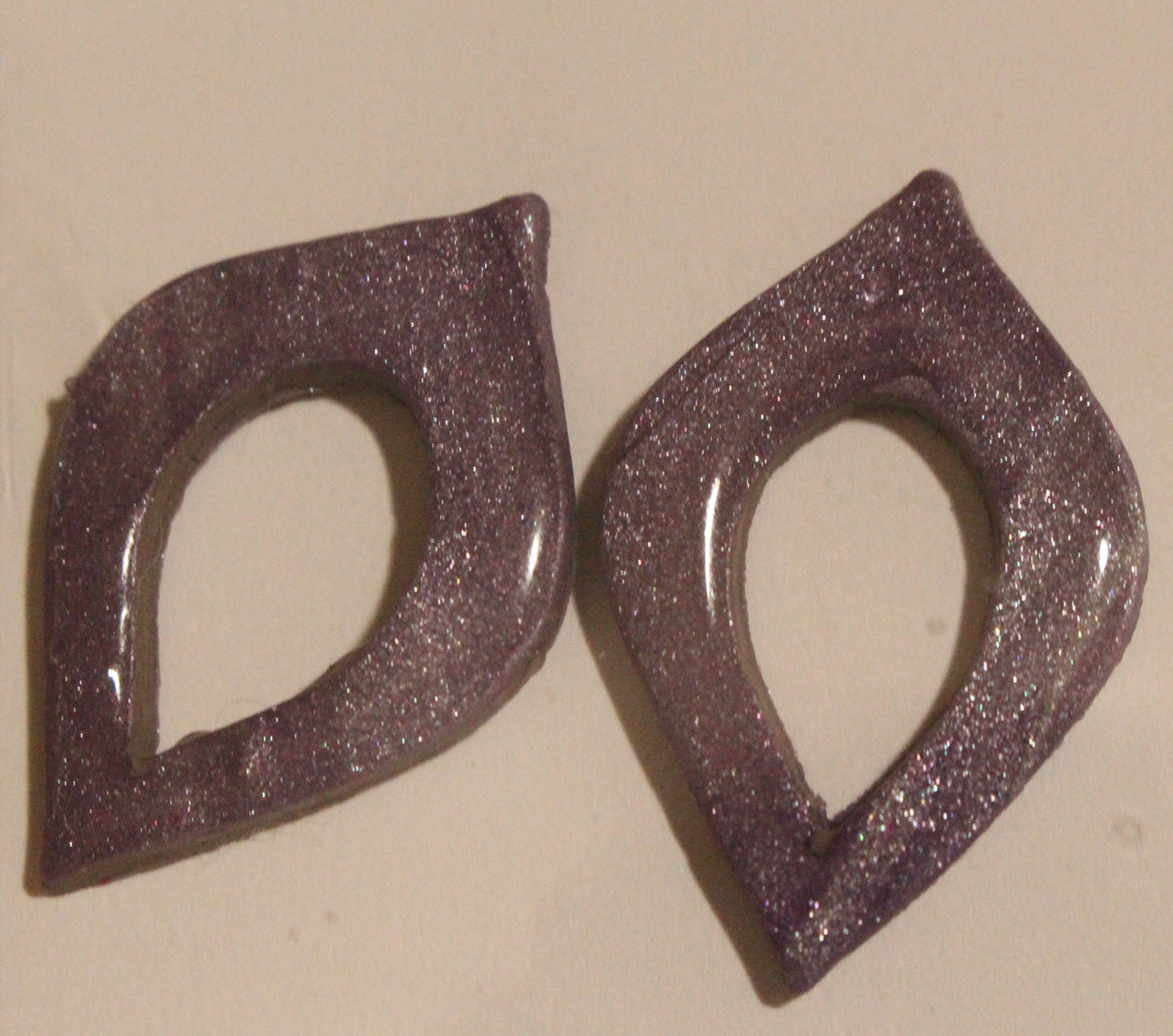 Pair of purple glittery earrings on a beige background