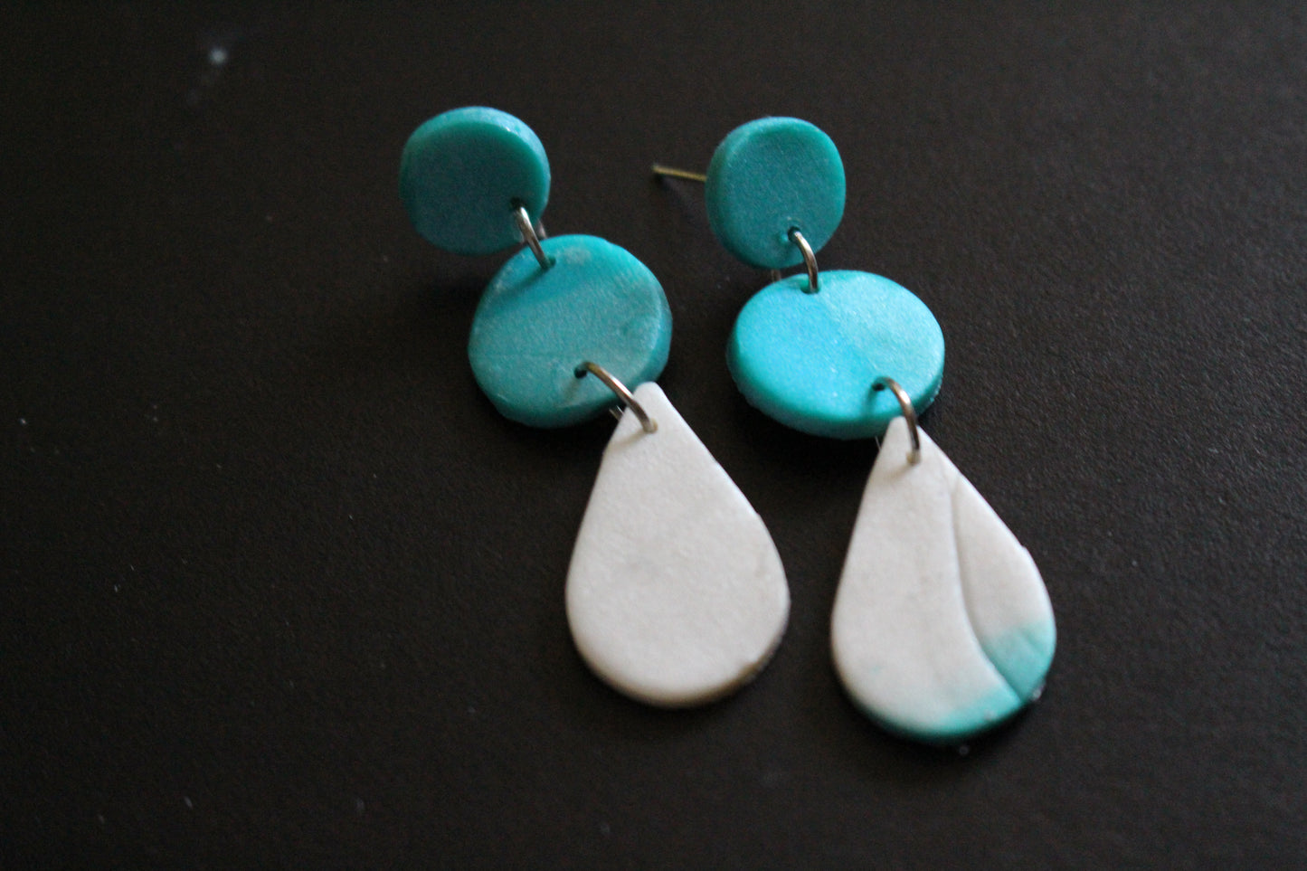 Turquoise and white ceramic earrings on a black background