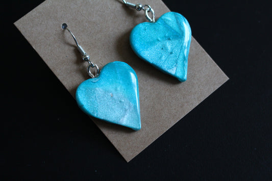 Turquoise heart-shaped earrings on a brown card against a black background