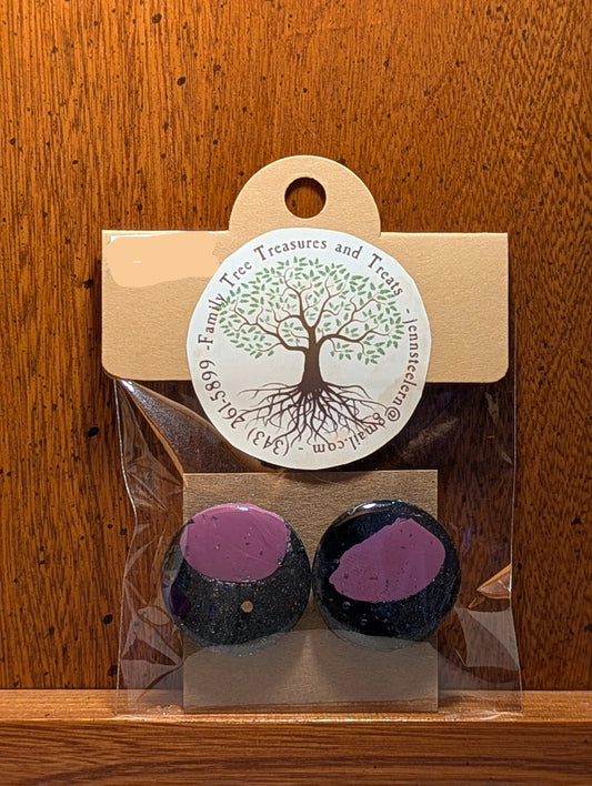 Two black and purple bath bombs in clear packaging with a tree label on a wooden surface.